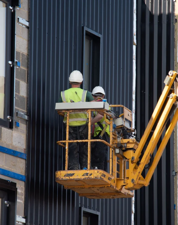Zwei Monteure auf einer Hebebühne vor einer Paneelfassade